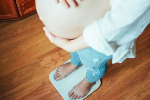 Image of woman weighing herself and experiencing weight gain through pregnancy Oxshott